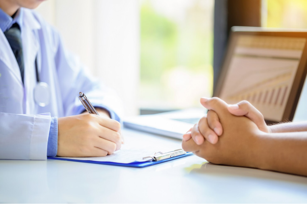 A close-up of a doctor taking notes while a patient with clasped hands sits across, symbolizing supportive outpatient rehab in Thousand Oaks, CA.