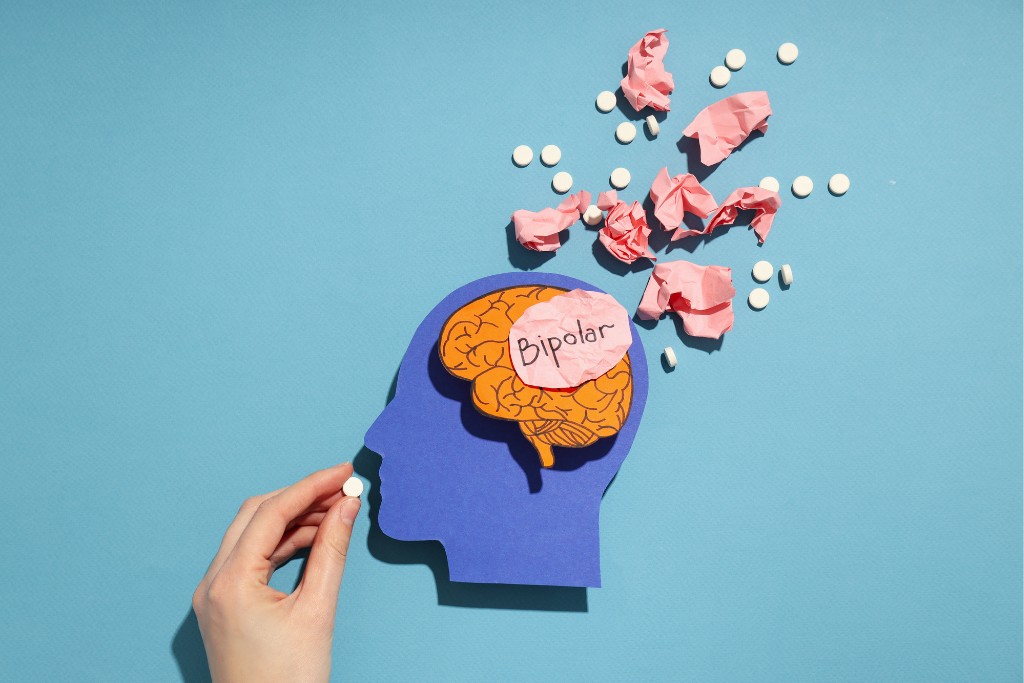 A hand holding a cutout of a head with "Bipolar" written on the brain, surrounded by crumpled paper and pills, representing the mental and physical aspects of bipolar disorder. This illustrates the comprehensive approach needed for bipolar treatment in Thousand Oaks, CA.