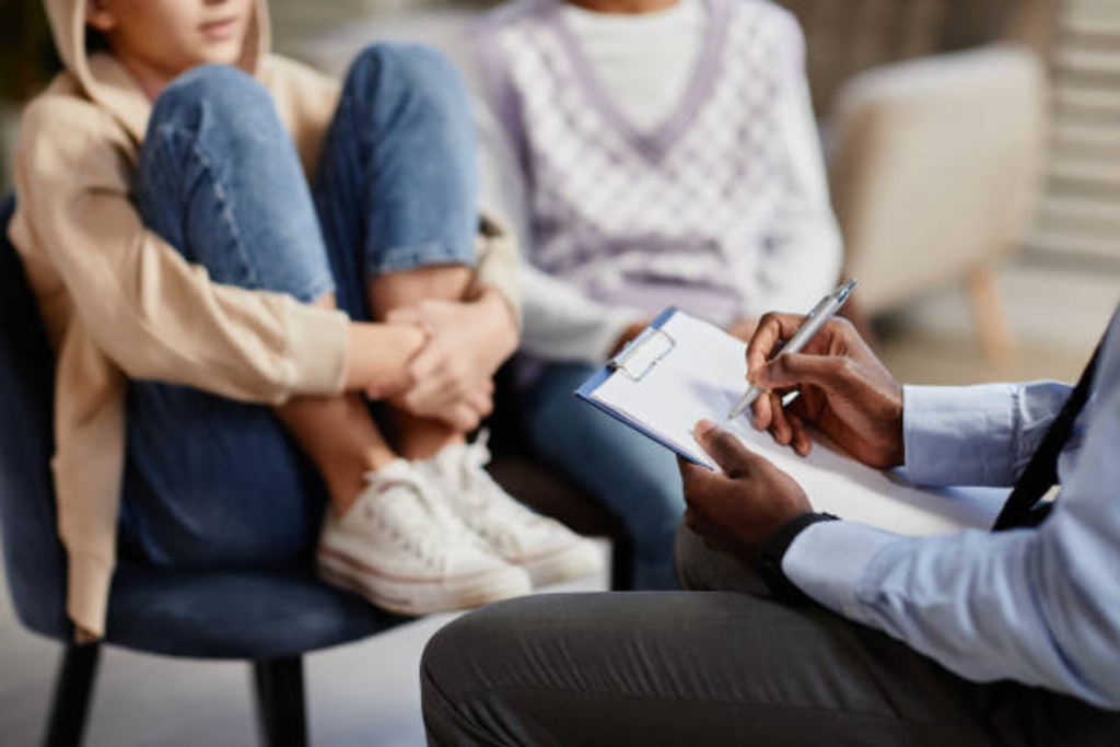 A therapist with a clipboard, talking to a young family during a family therapy session in Thousand Oaks, CA, fostering open communication.